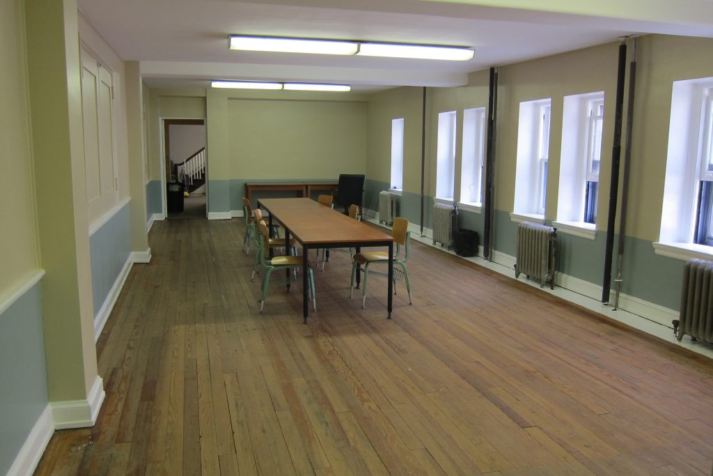 An image of a long narrow room with a long rectangular table with six chairs